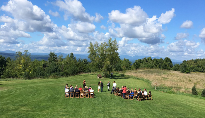 A wedding ceremony is held in front of a small audience in a meadow by Spring Farm with the Million Dollar View of the Catskills in the distance.