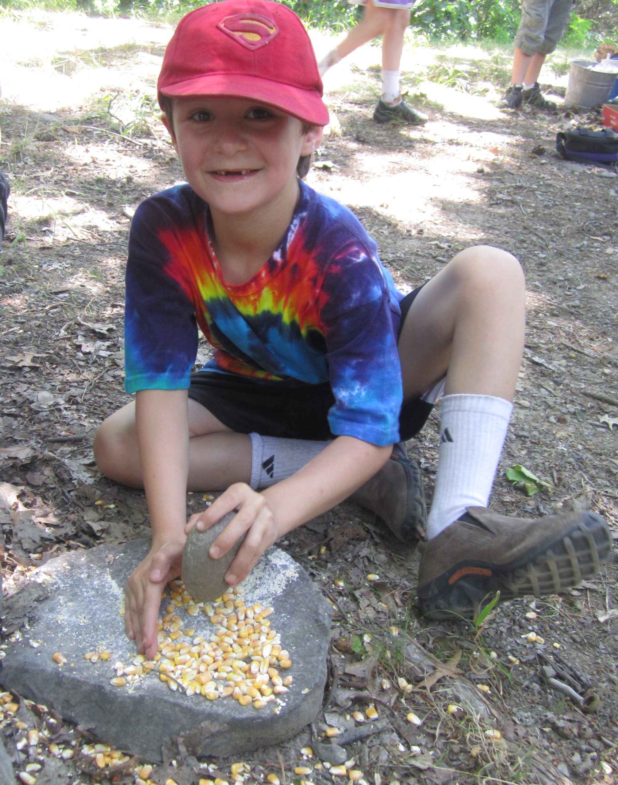 Young child with a pile of corn on a stone in a natural setting learning about historic Lenni Lenape traditions.